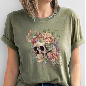 May include: A green t-shirt with a floral skull graphic. The skull is surrounded by pink, white, and purple flowers.