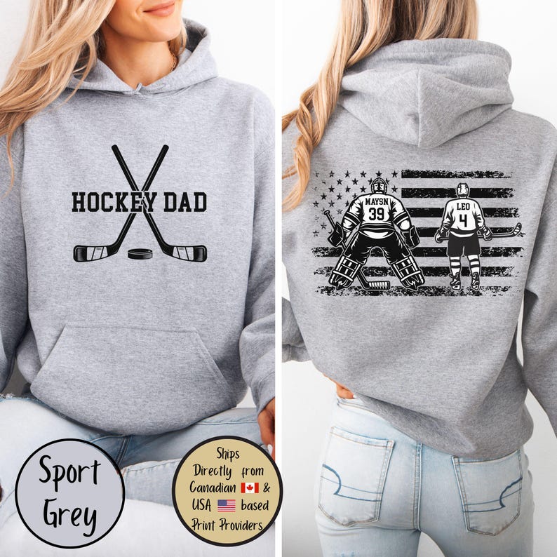 Puede incluir: Sudadera con capucha gris deportivo con texto "HOCKEY DAD" y gr&aacute;fico de palos de hockey en la parte delantera. La parte trasera presenta un gr&aacute;fico de portero y jugador de hockey con un dise&ntilde;o de bandera estadounidense.