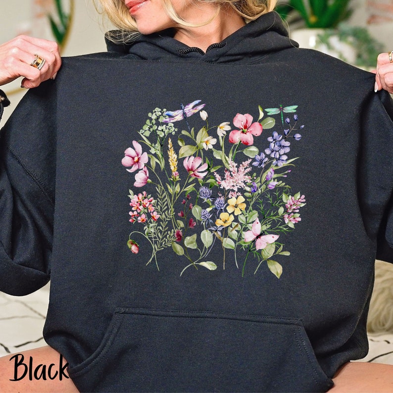 K&ouml;nnte beinhalten: Schwarzer Kapuzenpullover mit einem Blumendruck mit rosa, lila, gelben und wei&szlig;en Blumen, gr&uuml;nen Bl&auml;ttern und Libellen.
