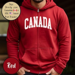 May include: Red zippered hoodie with the word "CANADA" in white letters across the chest.