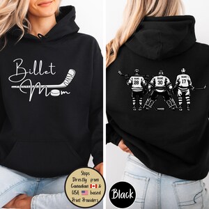 May include: Black hoodie with a front design that says "Billet Mom" with a hockey stick and puck. The back features a hockey team graphic with the word "NAME" above the numbers 28, 30, and 17. The hoodie has a front pocket and a hood.
