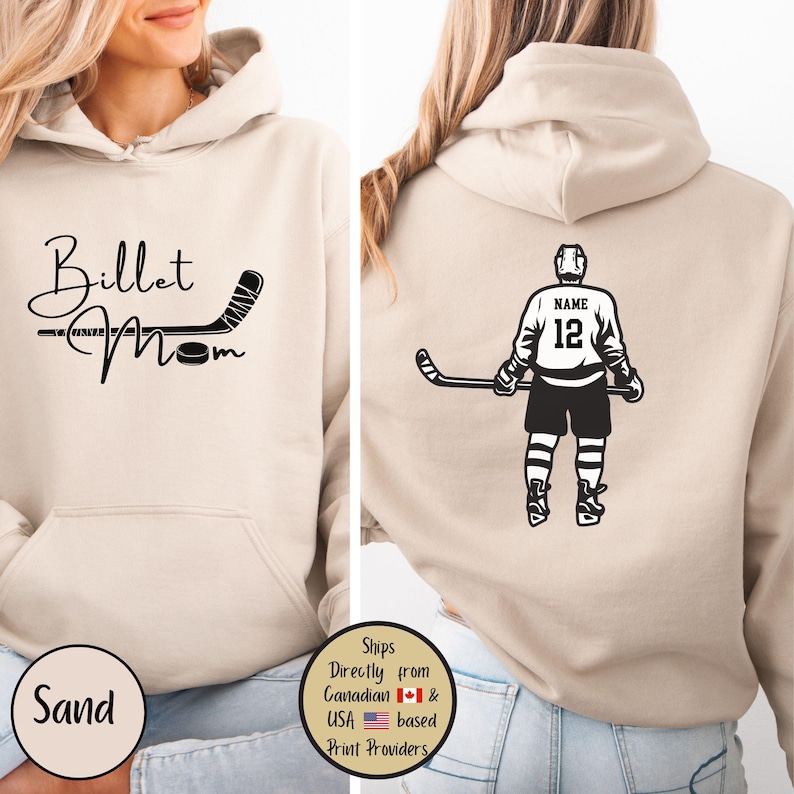 May include: Sand-colored hoodie with a hockey-themed design. The front features the text "Billet Mom" with a hockey stick and puck graphic. The back displays a hockey player with the number 12 and the word "NAME" above. A round label says "Sand".