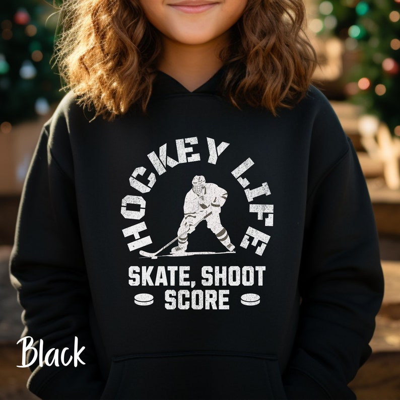 Op de afbeelding: Zwarte hoodie met een witte afbeelding van een hockeyer en de tekst "Hockey Life Skate, Shoot Score".