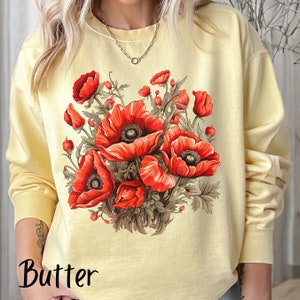 Peut inclure: Un sweat-shirt jaune avec un imprimé floral de coquelicots rouges. Le sweat-shirt a un col rond et des manches longues.
