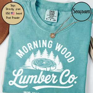 以下が含まれることがあります： 「Morning Wood Lumber Co.」という白いグラフィックデザインが施されたターコイズブルーのTシャツ。スタイリッシュな木と木目模様がデザインされています。このTシャツは柔らかく快適な素材で作られています。