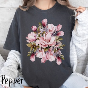 Peut inclure: Un t-shirt gris fonc&eacute; avec un motif floral compos&eacute; de fleurs de magnolia roses et blanches avec des feuilles vertes.
