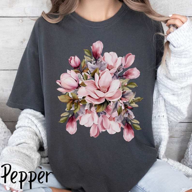 Peut inclure: Un t-shirt gris fonc&eacute; avec un motif floral compos&eacute; de fleurs de magnolia roses et blanches avec des feuilles vertes.
