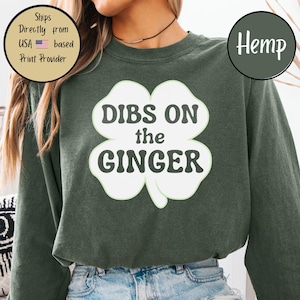 May include: Dark green sweatshirt featuring the text "DIBS ON the GINGER" in a white four-leaf clover design. The word "Hemp" is in a green circle. The sweatshirt is a casual style.