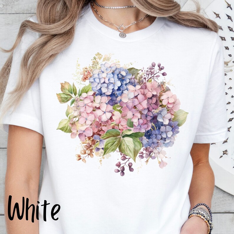 Peut inclure: T-shirt blanc avec un motif floral aquarelle de hortensias roses, bleus et violets.