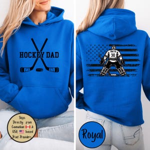 Puede incluir: Sudadera con capucha azul real con el texto "HOCKEY DAD" y palos de hockey cruzados y un disco. La parte trasera presenta un gr&aacute;fico de portero de hockey con el nombre "Smith" y el n&uacute;mero "30" sobre un dise&ntilde;o de bandera estadounidense desgastada.