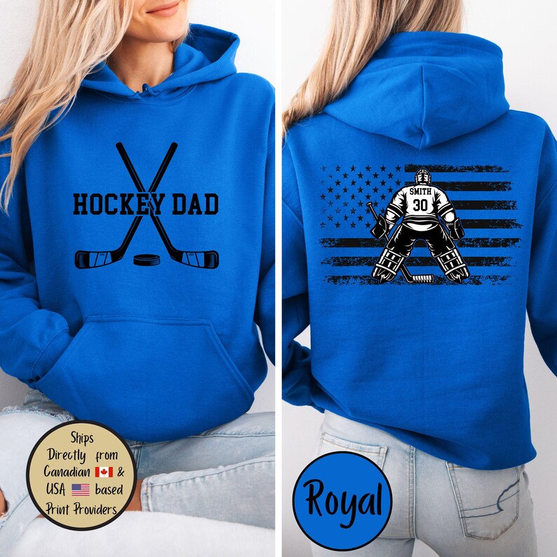 Puede incluir: Sudadera con capucha azul real con el texto "HOCKEY DAD" y palos de hockey cruzados y un disco. La parte trasera presenta un gr&aacute;fico de portero de hockey con el nombre "Smith" y el n&uacute;mero "30" sobre un dise&ntilde;o de bandera estadounidense desgastada.