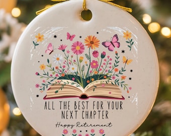 May include: Round ceramic ornament with a floral and butterfly design. The ornament features an open book with colorful flowers and butterflies. Text reads "ALL THE BEST FOR YOUR NEXT CHAPTER Happy Retirement."