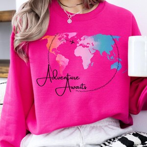 May include: Pink sweatshirt with a watercolor world map design and the text "Adventure Awaits".