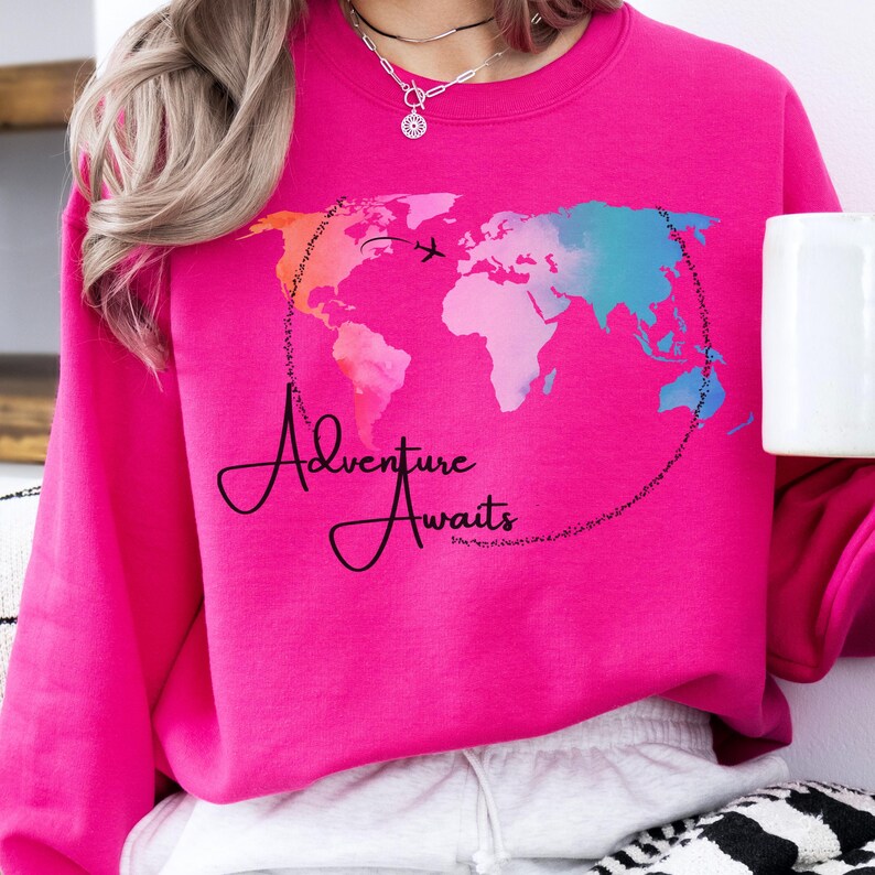 May include: Pink sweatshirt with a watercolor world map design and the text "Adventure Awaits".