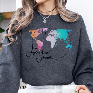 May include: A dark gray sweatshirt with a watercolor world map design and the text "Adventure Awaits".