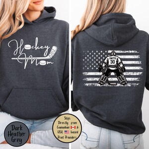 May include: Dark heather grey hoodie with the text "Hockey Mom" and a hockey stick and puck graphic. The back features an American flag design with a hockey goalie and the name "Smith" and the number "30".