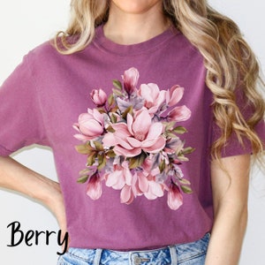 Peut inclure: Un t-shirt mauve avec un imprim&eacute; floral de fleurs de magnolia roses et blanches avec des feuilles vertes. Le mot "Berry" est imprim&eacute; en noir en bas &agrave; gauche de l'image.