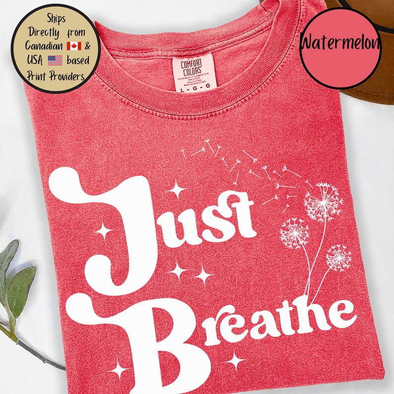 May include: A red t-shirt with the words "Just Breathe" in large white letters. The shirt features a dandelion design and the colour is labelled "Watermelon". The shirt is a Comfort Colors brand.