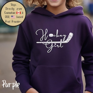 May include: A purple hoodie with a front pocket. The hoodie features the white text "Hockey Girl" with a hockey stick and puck graphic. The word "Purple" is at the bottom left.