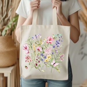 May include: A white canvas tote bag with a floral design. The design features pink, purple, yellow, and blue flowers, green leaves, and two dragonflies.