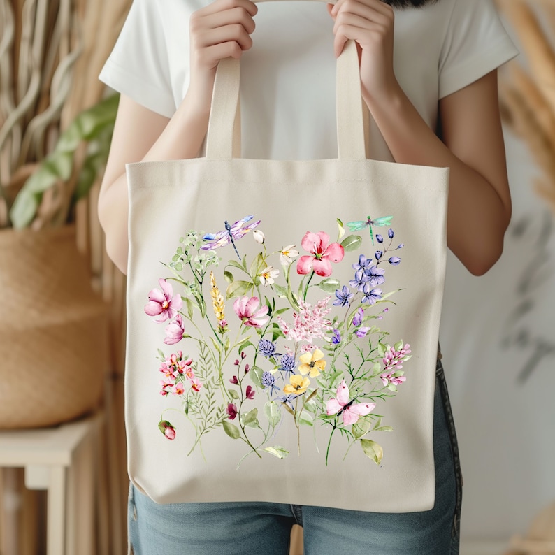 May include: A white canvas tote bag with a floral design. The design features pink, purple, yellow, and blue flowers, green leaves, and two dragonflies.
