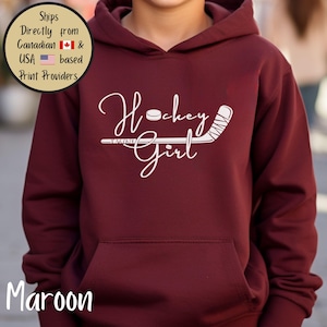 May include: Maroon hoodie with a white "Hockey Girl" design featuring a hockey puck and stick. The hoodie has a front pocket and a hood. The word "Maroon" is printed at the bottom of the image.