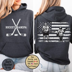 Peut inclure: Sweat à capuche gris foncé avec l'inscription "HOCKEY GRANDPA" et des crosses de hockey sur le devant. Le dos présente un drapeau américain avec des joueurs de hockey portant les numéros 19 et 91. Un haut décontracté pour les fans de hockey.