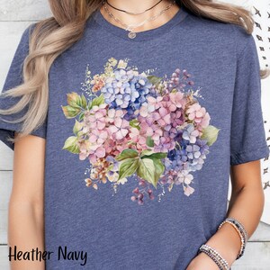 Peut inclure: Un t-shirt bleu marine chin&eacute; avec un motif floral aquarelle repr&eacute;sentant des hortensias roses et bleus.
