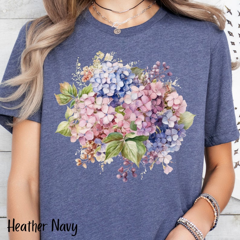 Peut inclure: Un t-shirt bleu marine chin&eacute; avec un motif floral aquarelle repr&eacute;sentant des hortensias roses et bleus.