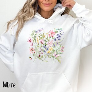 K&ouml;nnte beinhalten: Wei&szlig;er Hoodie mit einem Blumenmuster mit rosa, lila, gelben und gr&uuml;nen Blumen, Bl&auml;ttern und Libellen.