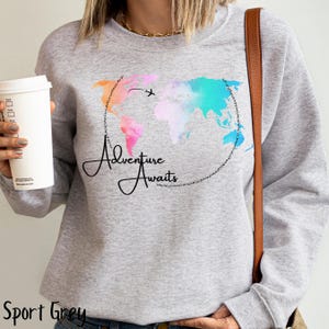 May include: A light gray sweatshirt with a watercolor world map design and the text "Adventure Awaits" in black script.