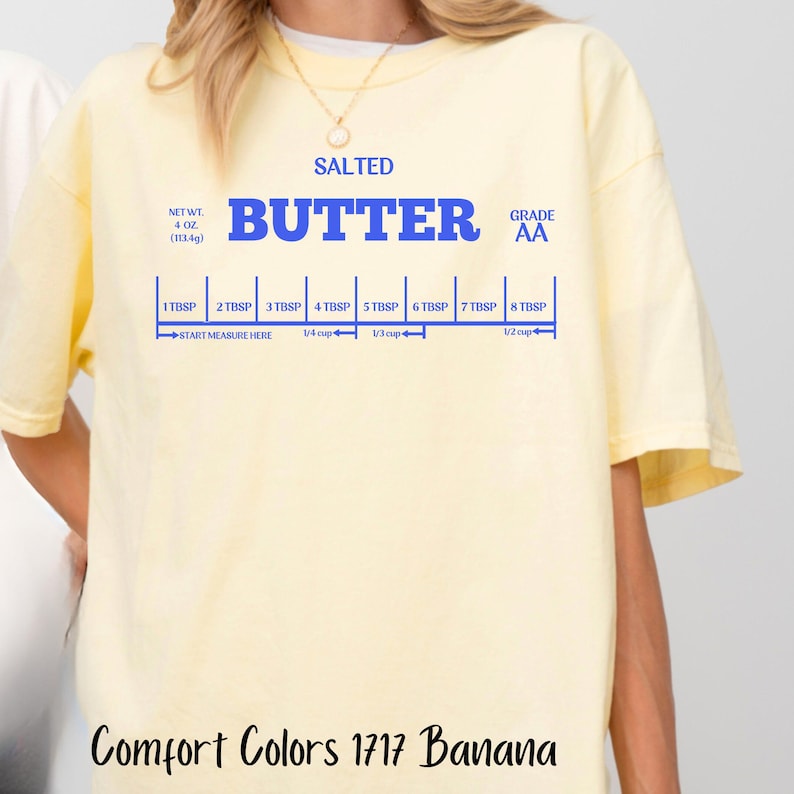 May include: A yellow t-shirt with the words "SALTED BUTTER GRADE AA" printed in blue. The shirt also has a blue ruler with measurements in tablespoons and cups.