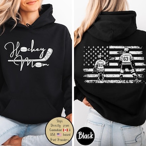 May include: Black hoodie with a front design that says "Hockey Mom" in white script with hockey stick and puck graphics. The back features an American flag design with hockey players and the number 63.