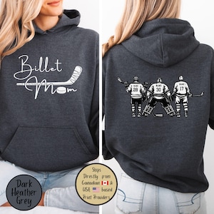 May include: Dark heather grey hoodie with a front graphic that says "Billet Mom" with a hockey stick and puck. The back features a hockey team graphic with player numbers and names. The hoodie has a hood and a front pocket.