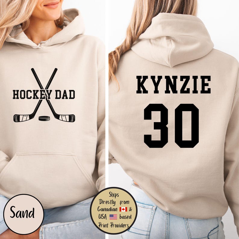 Puede incluir: Sudadera con capucha color arena con el texto "HOCKEY DAD" y palos de hockey cruzados en la parte delantera. La parte trasera presenta el nombre "KYNZIE" y el n&uacute;mero "30" en negro. Prenda de vestir informal y c&oacute;moda.
