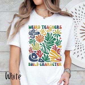 May include: White t-shirt with a colourful abstract design and the text "Weird Teachers Build Character".