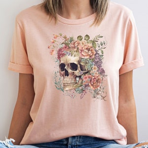 May include: A pink t-shirt with a floral skull design. The skull is surrounded by pink, white, and purple flowers.