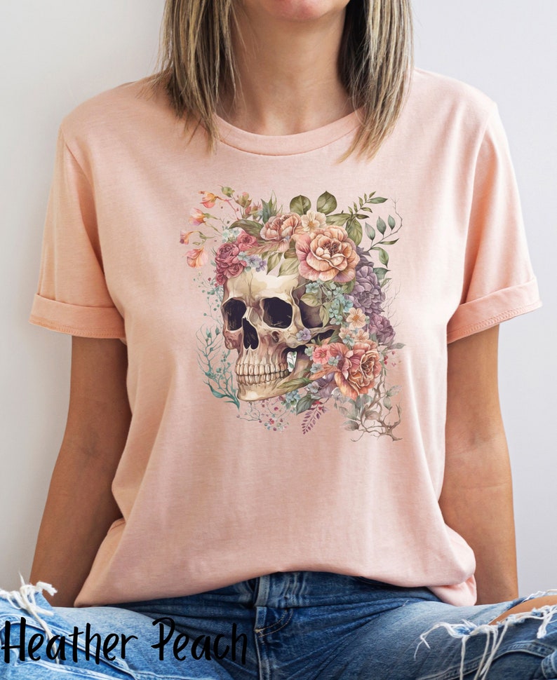 May include: A pink t-shirt with a floral skull design. The skull is surrounded by pink, white, and purple flowers.