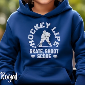 Op de afbeelding: Koninklijk blauwe hoodie met een witte afbeelding van een hockeyer in een cirkel met de tekst "Hockey Life" en "Skate, Shoot Score" eronder.
