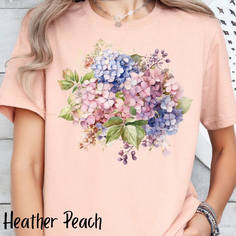 Peut inclure: Un t-shirt en p&ecirc;che bruy&egrave;re avec un motif floral aquarelle repr&eacute;sentant des hortensias roses, violets et bleus.