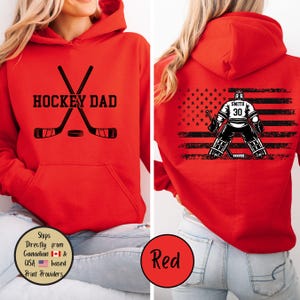 Puede incluir: Sudadera con capucha roja con "HOCKEY DAD" en letras negras, palos de hockey cruzados y un disco. La parte trasera presenta un gr&aacute;fico de portero de hockey con el nombre "SMITH" y el n&uacute;mero "30" sobre un dise&ntilde;o de bandera estadounidense en blanco y negro.