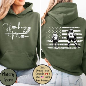 May include: Military green hoodie with the text "Hockey Mom" in white script on the front. The back features an American flag design with two hockey players and the name "Lambert" and the number "63".