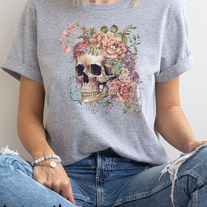 May include: A gray t-shirt with a floral skull design. The skull is surrounded by pink, white, and purple flowers.