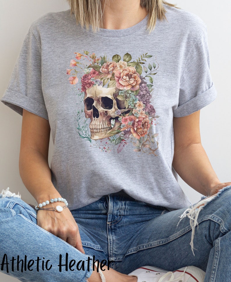May include: A gray t-shirt with a floral skull design. The skull is surrounded by pink, white, and purple flowers.