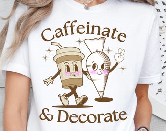 May include: White t-shirt with a brown graphic of a coffee cup and a piping bag with the text "Caffeinate & Decorate".