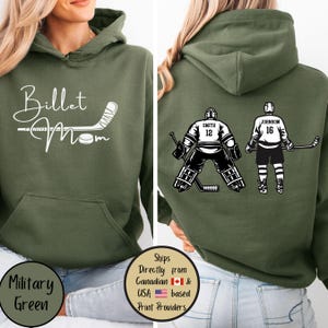 May include: Military green hoodie with the words "Billet Mom" and a hockey stick and puck graphic. The back features hockey player illustrations with the names Smith and Johnson and the numbers 12 and 16. The hoodie has a front pocket.