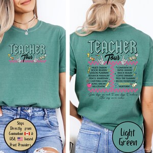 May include: Light green t-shirt with the text "Teacher Tour" in a stylized font, featuring graphics of hands, pencils, and musical notes. The back of the shirt lists teacher-related activities. The shirt is made of a soft material.