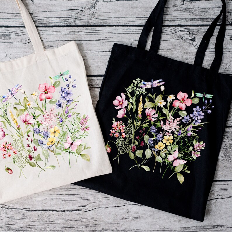 May include: Two tote bags with floral designs. One bag is white with a floral design in shades of pink, purple, and green. The other bag is black with a floral design in shades of pink, purple, and green.