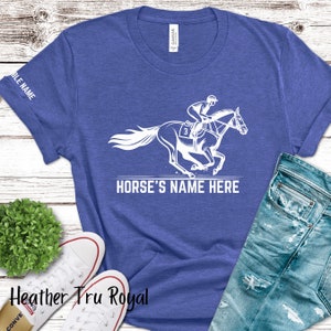 May include: A blue t-shirt with a white design of a jockey riding a horse. The text "HORSE'S NAME HERE" is printed below the design.