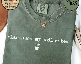 Peut inclure: Un t-shirt vert mousse avec le texte "plants are my soil mates" en blanc. Un petit graphique de plante en pot se trouve sous le texte.